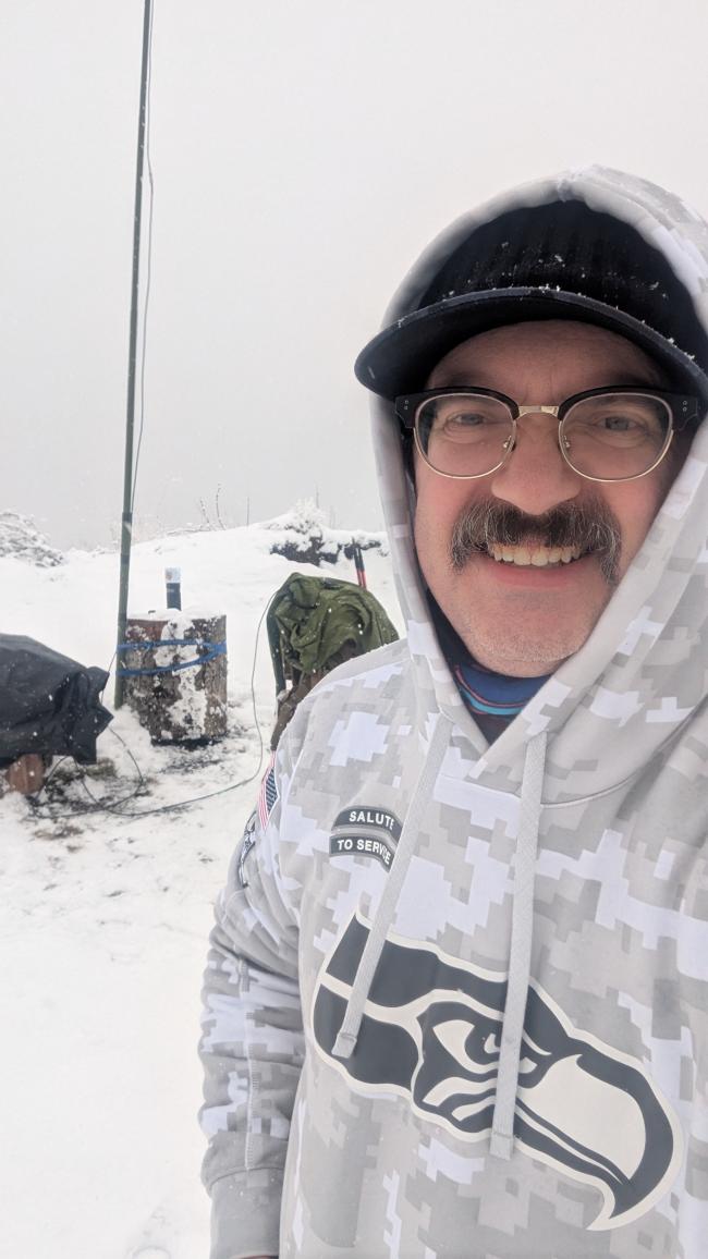 man standing in front of portable ham-radio setup in the snow, smiling