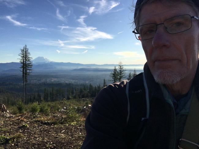 Selfie against clearcut and blue sky with Tahoma (Mt Rainier) in the background.